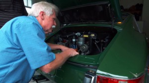 man looking at engine in back of old green hatchback car